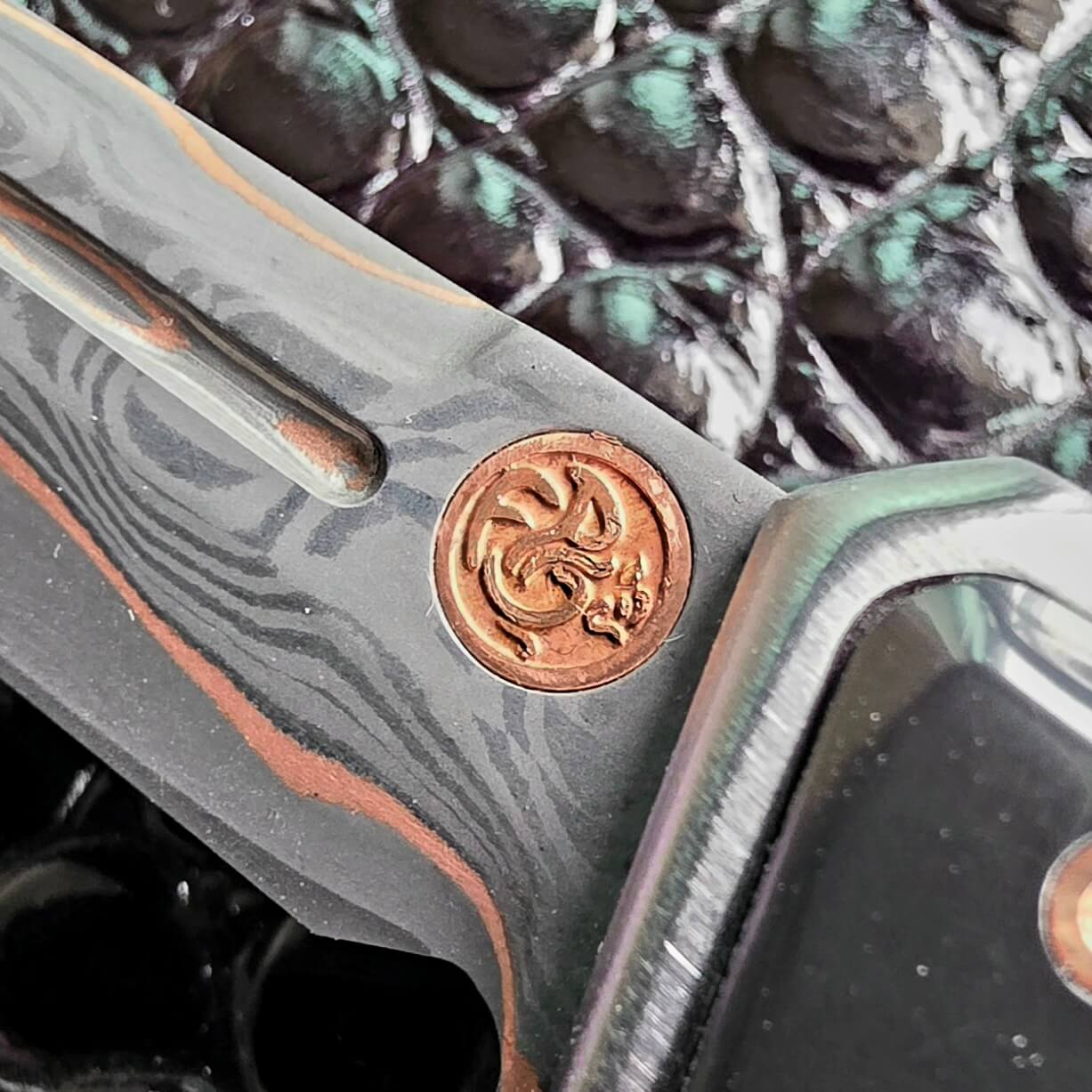 Copper maker’s mark medallion inlaid into the blade flat of the Patrick Famin Mother of Pearl G.O.T.F. Mini, beside the fuller