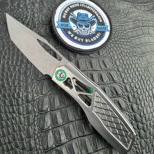 Prince Customs Protean Skelly Dragon open on its show side beside the We Buy Knife Collections patch