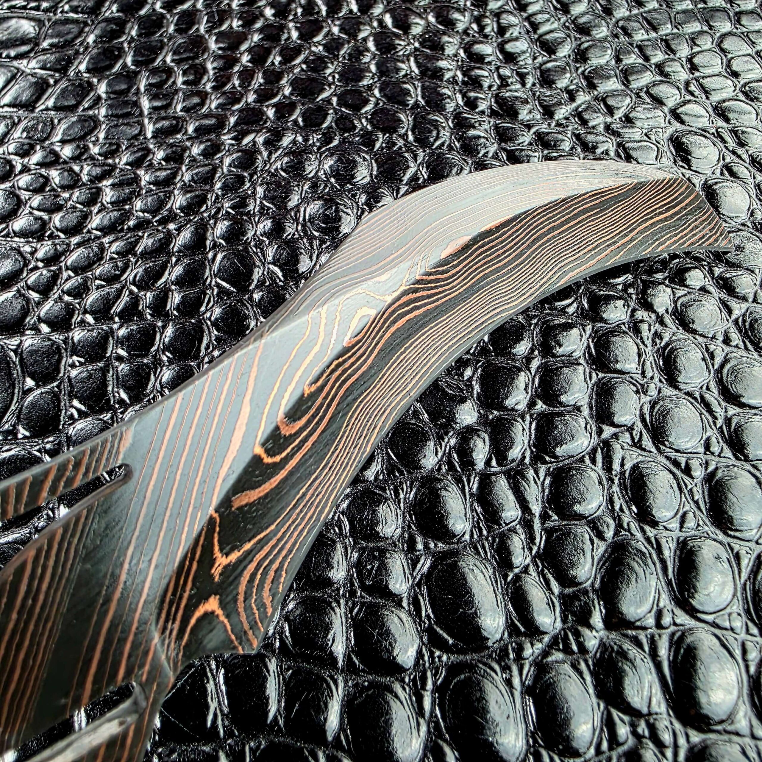 Close view of the Reese Weiland Harpy hawkbill curve, with Copper lines running through the Damascus