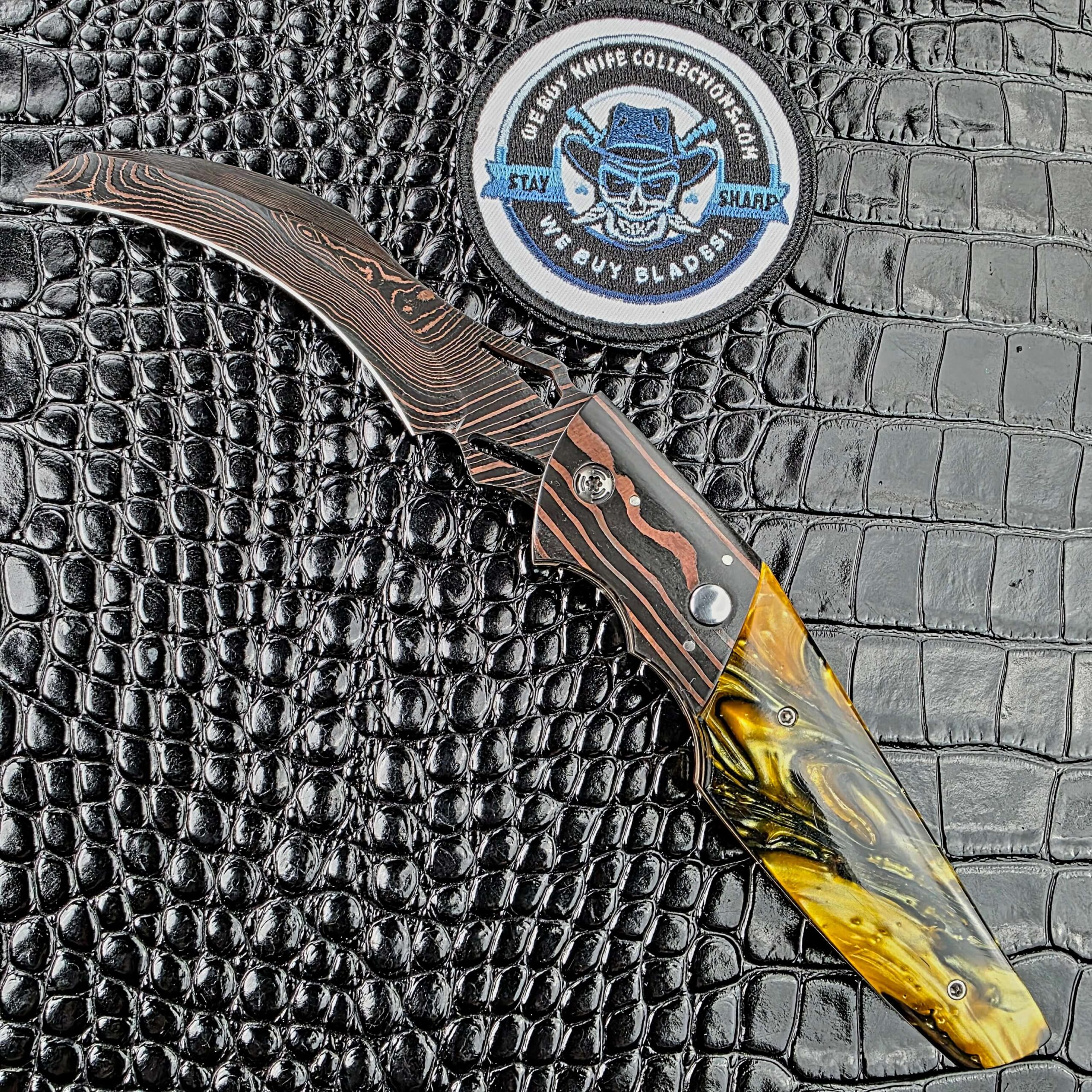 Reese Weiland Harpy open on its show side with a Brad Vice Copper Damascus hawkbill and Honey Hive Acrylic scale beside the We Buy Knife Collections patch