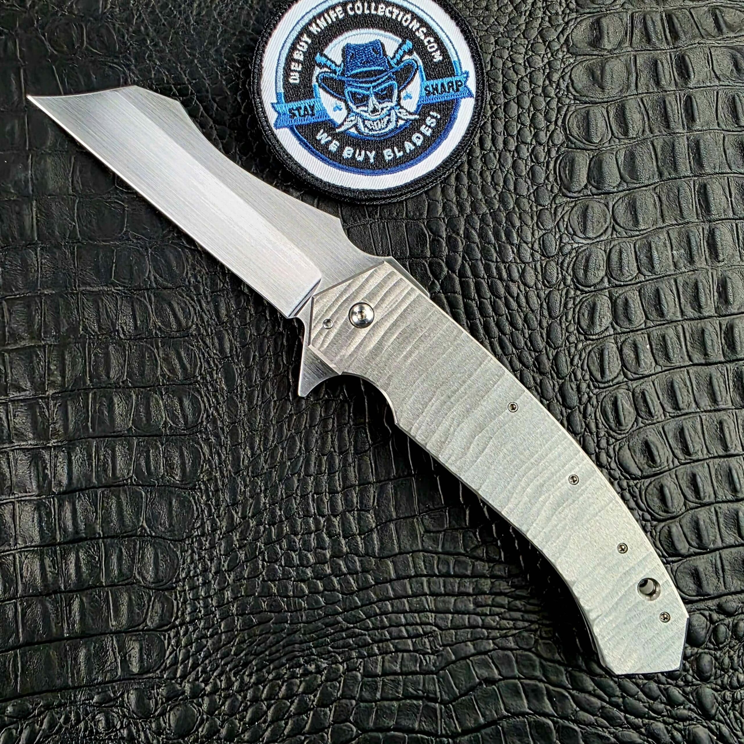 Reese Weiland Strike Prototype 2 open on its show side beside the We Buy Knife Collections patch